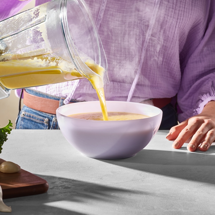 person pouring hot soup into bowl from blender