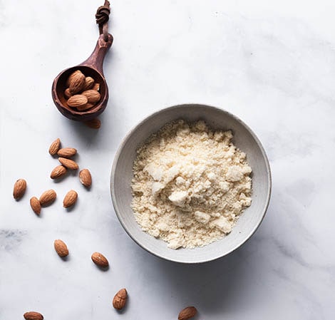 almond flour in a white bowl with whole almonds scattered around