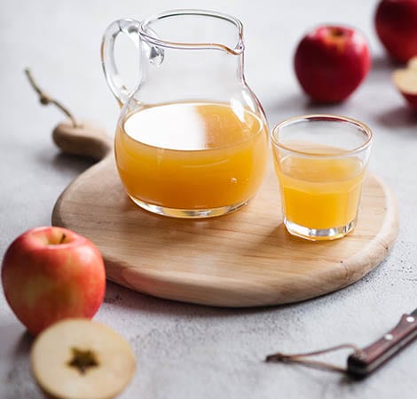 裝著蘋果汁的玻璃壺與一杯蘋果汁放在木盤上