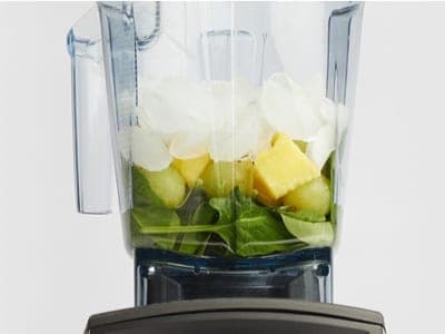 A blender loaded with spinach, pineapple and ice