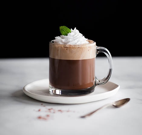 玻璃马克杯中的咖啡饮品泛着泡沫和掼奶油，用薄荷叶子作装饰