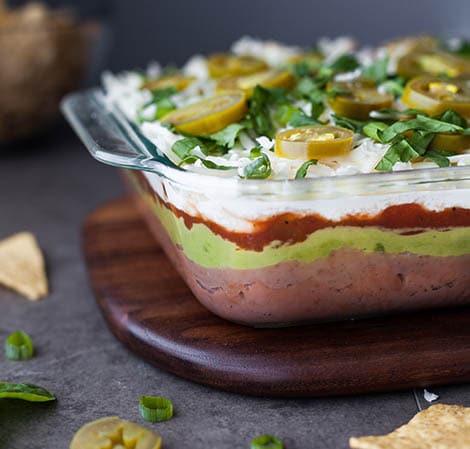 Seven layer taco dip in a clear baking dish with a chip off to the side.