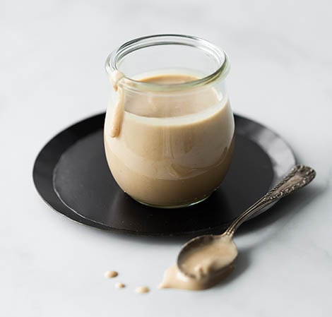 Tahini in a glass jar with a spoon on the side
