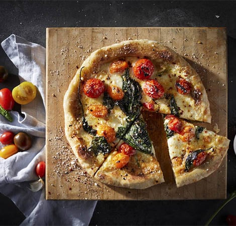 Pizza mit Basilikum und Tomaten belegt auf einem Schneidebrett